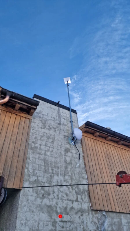 Antenna Starlink montata su parete esterna di abitazione con rivestimento in legno e muro in pietra, cielo sereno sullo sfondo