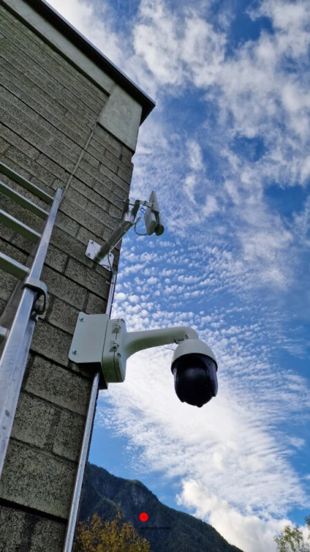Telecamere di videosorveglianza PTZ montate su parete esterna in cemento con sfondo montuoso e cielo nuvoloso