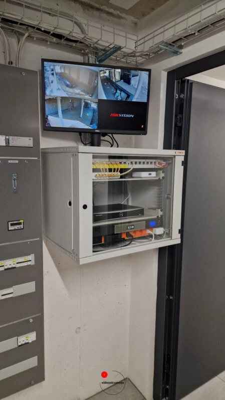 Armadio rack a muro contenente registratore NVR e router, con monitor che mostra le riprese delle telecamere di videosorveglianza interne