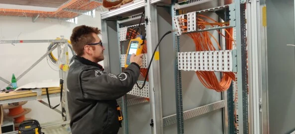 Operatore specializzato effettua misurazioni con strumento di rete su pannello di distribuzione con cavi strutturati in rame, all’interno di sala tecnica